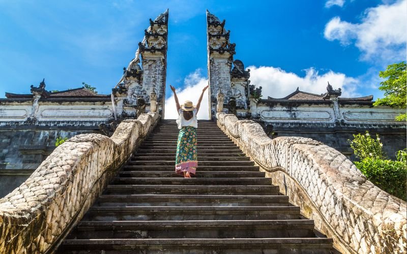 lady walking up steps with her arms up in the air as she approaches a beautiful Balinese gate