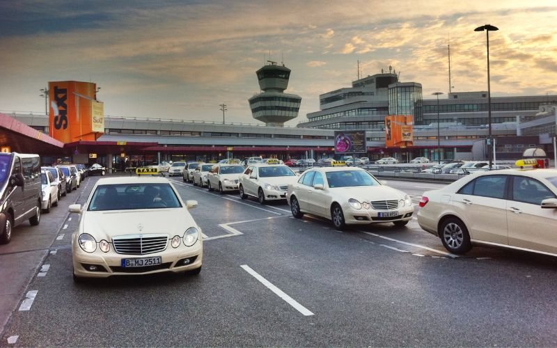 taxis driving in a row on a road leading into an airport