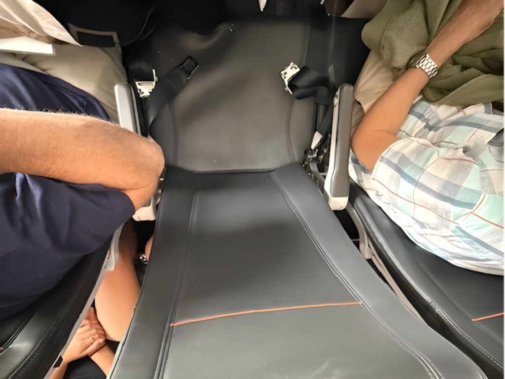 aerial view from above looking down onto an econonmy aeroplane seat that is grey leather with orange piping with a seat belt