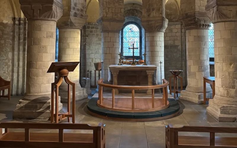 inside of an old church featuring decorative stone pillars and an altar with brown wooden pews and a stained glass window in the background