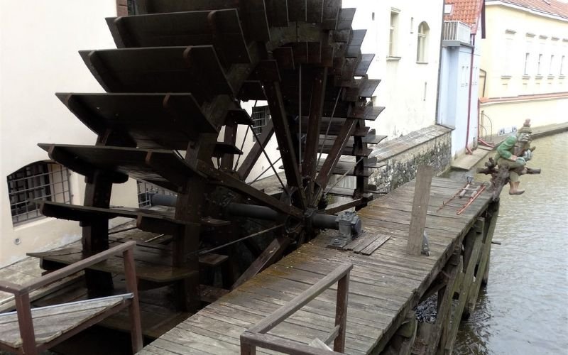 large brown wooden waterwheel with a river beneath and a small wooden landing next to it