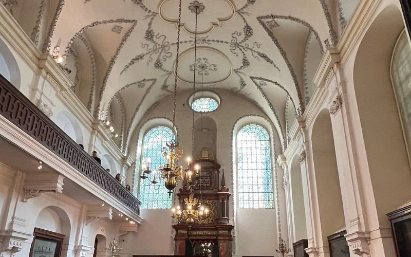 decorative interior of a church with high arch windows, chandeliers and a wooden balcony