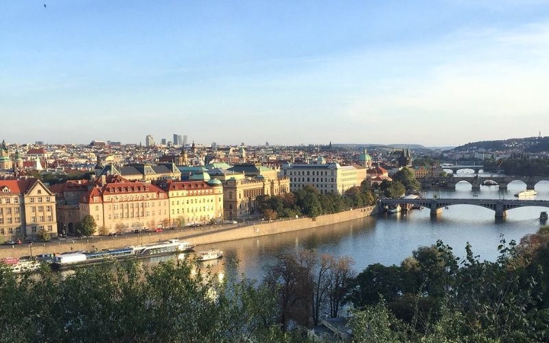 sweeping views of a large river surrounded by historic buildings and wide bridges with the glowing sun in the background