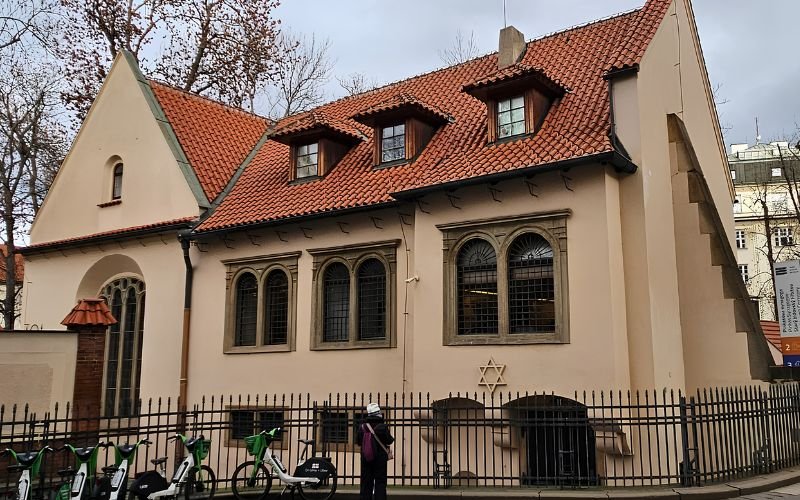 historic synagogue with a terracotta tiled roof and black fence around it.