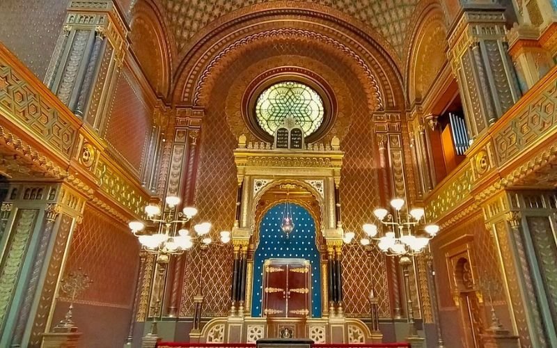 intricate details of the inside of a Spanish Synagogue featuring a large gold chandelier and walls covered in tiny gold and aqua blue mosaic tiles