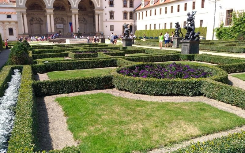 green manicured gardens with dark green hedging and squares of green grass with a majestic building in the background with large arches