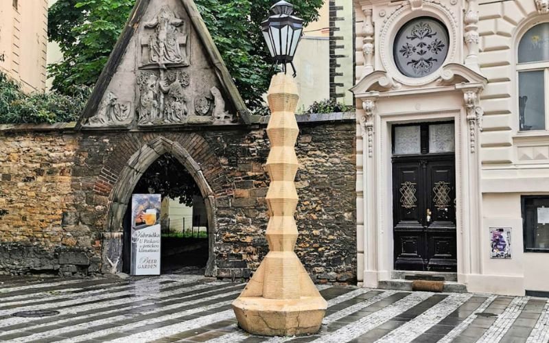 sandstone tall cubist lampost surrounded by a courtyard with old arched buldings sitting on a cobblestone flooring