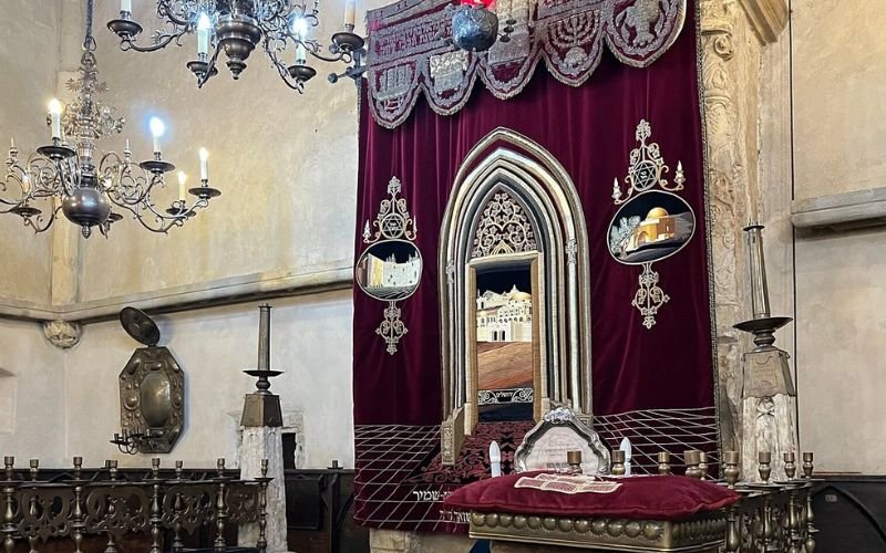 interior of an old synagogue with burgundy velvet drapes, soft chandelier lighting, arched mirror and and a gold altar