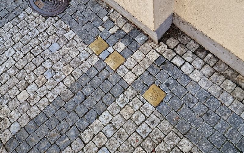light grey and dark grey small square cobblestones with three gold plague stones showing the name of Jews killed